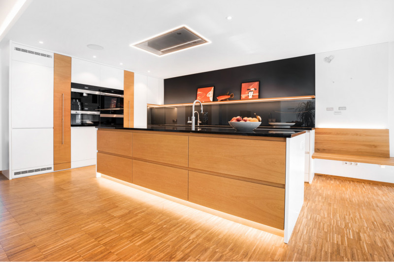 Designküche nach Maß mit einer zentralen Kochinsel aus Holz mit grifflosen Schubladen, einer schwarzen Küchenrückwand und einer passenden Sitzbank.