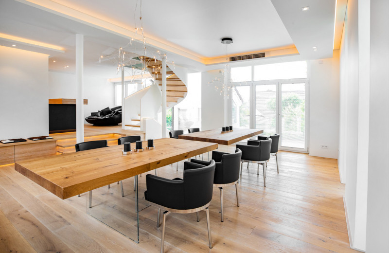 Heller Essbereich als Teil eines kompletten Innenausbaus. Zentral ein massiver Holztisch auf Glasbeinen schwebend.